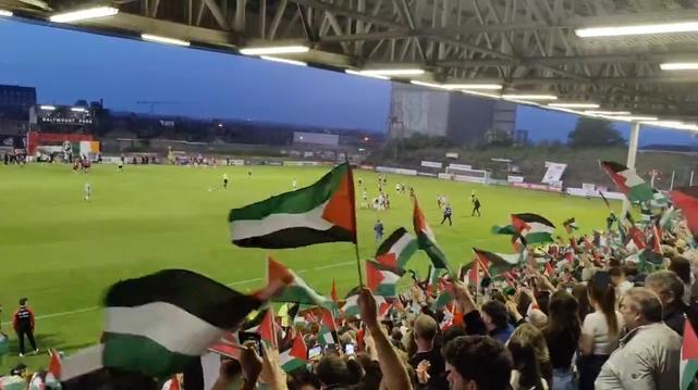 It's full time. Soccer field,  seen from stand with everyone going berserk waving Palestine flags