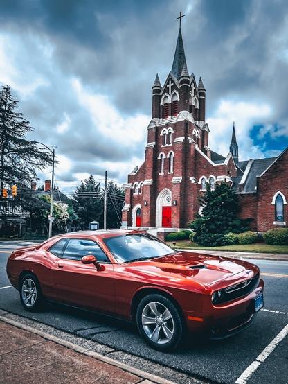 Orange-metallic-farbender Dodge Challenger vor einer Kirche