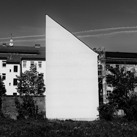 Blick auf eine weiss getünchte sonnenbeschienene Brandmauer eines Gebäudes. Im Hintergrund eine Häuserreihe