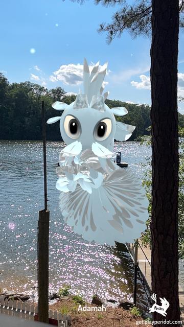 A white and pastel blue dot with the plumage chaos trait Grassy Blades hovering in the air with a lake in the background and a pine tree to the right.