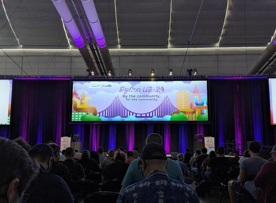 Photo from the PyCon keynote audience before the first keynote, the screen showing the PyCon 2024 illustration