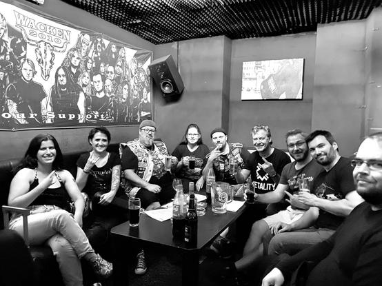 Foto einer Gruppe personen, die in einem Loungebereich einer Bar um einen niedrigen Tisch herum aufSofas sitzen. Auf dem kleinen Tisch befinden sich Getränke