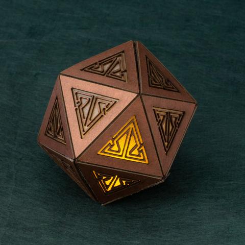 A small (~6cm / 2.25”) copper icosahedron with a key pattern cut into each face is lit from within by a yellow light.  It sits on a dark green background.