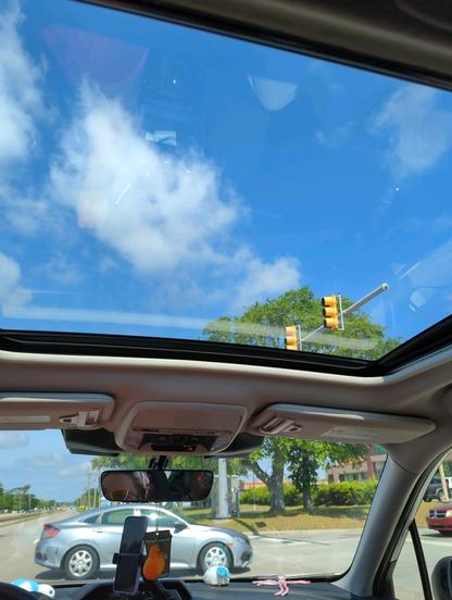 Blue sky and puffy clouds through the sun roof of a Subaru Forester.