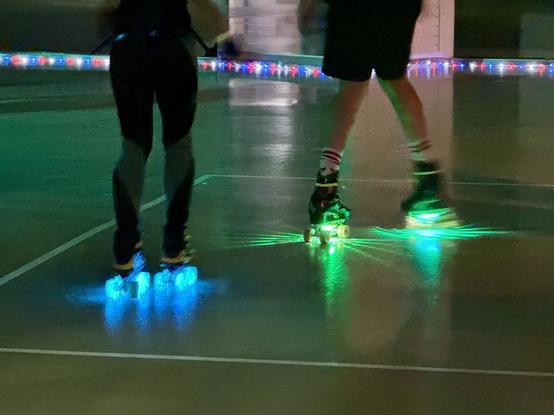 Zwei Personen skaten drinnen mit beleuchteten Rädern in einer beleuchteten Umgebung.