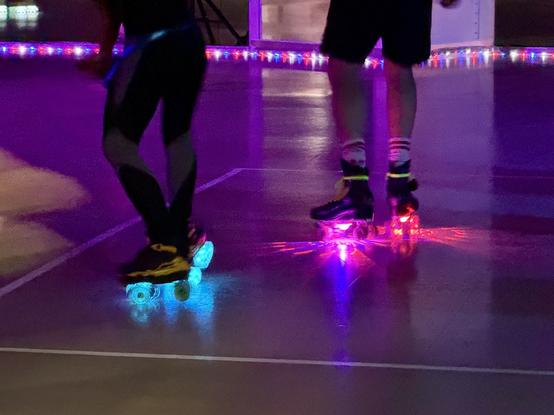 Zwei Personen skaten drinnen mit beleuchteten Rädern in einer beleuchteten Umgebung.