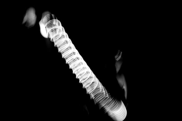 A movement of florescent slinky in a black-light performance set to music is captured in a blurred swirl.