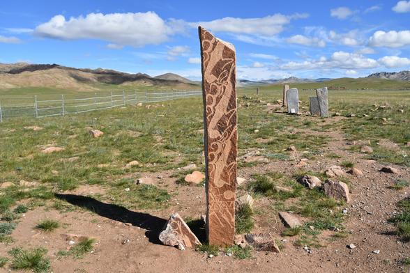 Une stèle monolithique s'élève sur la plaine mongole. Elle porte des gravures représentant des cerfs stylisés.
