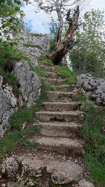 Escalier tournant bétonné, qui contourne un rocher. En haut à droite, un arbre mort. Encore plus haut, encore un rocher muni d'un garde-fou.