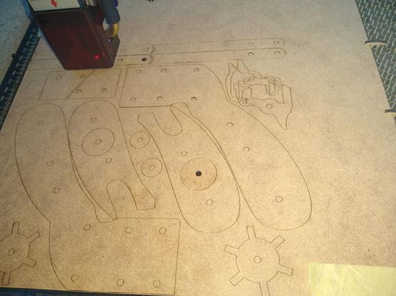 A laser cutter cutting out my new river band gun design on 2mm MDF board. You can see all the parts - body, handle, trigger mechanism and "barrel" as the laser traces the design. The trigger mech is a bit wobbly because I redesigned it on the fly.