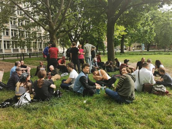 People sitting/standing around a park in smaller groups