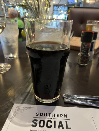 A glass of dark beer stands atop the menu from Southern Social MN restaurant