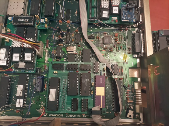 Populated and connected board. All ROMs are in. Later I changed the top/bottom 32K jumper into a wire to C128 Kernal switcher latch, so that JiffyDOS/DolphinDOS Kernal and 1571 DOS ROMs are switched simultaneously.
The ribbon cable is routed to the back, under the power supply to go out of the user port and back into user port plug.