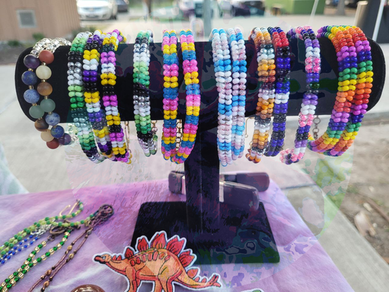 A group of bracelets hanging from a stand. The furthest two are chakra bracelets, the other pride flag themed.