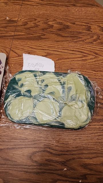 A mould of bear and paw shaped cold process soap with plastic wrap curing on a wooden table. There's a note of 5/20/24 22:00 for when it was set.