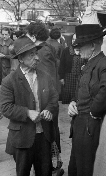 A black and white photo of two older men standing facing each as if in conversation.