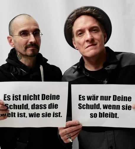 Mark Benecke und Bela B. mit Schildern: es ist nicht deine Schuld, dass die Welt ist, wie sie ist. Es wäre nur deine Schuld, wenn sie so bleibt.