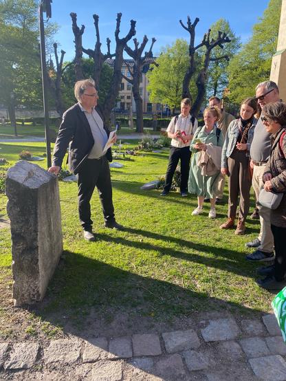 Magnus Källström standing in front of the Liljegren gravestone speaking to a crowd of people.