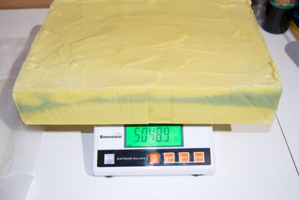 Un gros pain de savon en saponification à froid est posé sur une balance de précision. Il pèse 5048,9 grammes. 
Le savon est jaune citron avec une trace de vert. Le jaune, c'est la couleur de l'huile de colza !