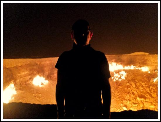 A silhouetted figure stands before a fiery crater in the dark.