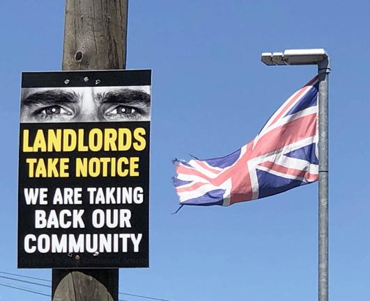 On the left, a placard on a power pole with a pair of eyes and the words "Landlords, take notice – we are taking back our community". On the right, a Union Flag. A blue sky forms the background