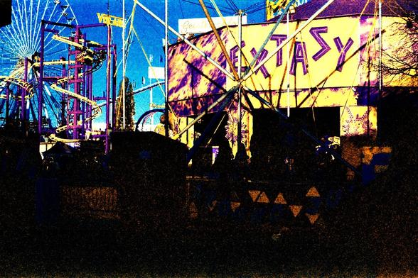 Besuch im Prater in Wien am Abend. Das Bild zeigt mehrere Stände - darunter ganz links das Riesenrad, rechts davor etwas Gerüstähnliches, ganz rechts etwas namens Extasy. Verfremdete Farben wegen des abgelaufenen Films.
