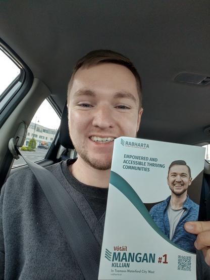 A photo of me smiling in my car holding a leaflet.