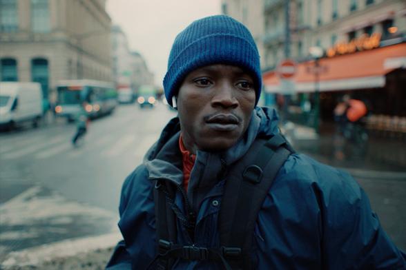 A Black man in a blue woolly hat and coat looks stressed in The Story Of Souleymane