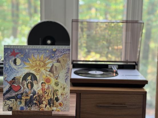 Tears for Fears - The Seeds of Love LP cover.

A drawing, in a relatively psychedelic style, of Roland and Curt in front of a huge sun and landscape, with Roland holding an umbrella.

The black LP plays on a vintage Bang & Olufsen Beogram 4000 linear-tracking turntable to the right.
