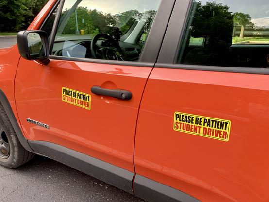 An orange car with a student driver magnet on each door.