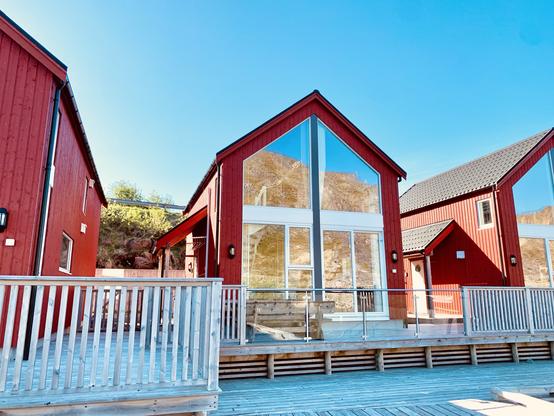 Red wooden cottages with large windows, a railing in the foreground, and blue skies above.