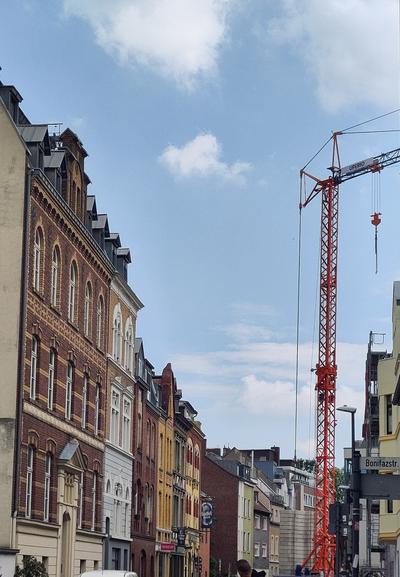 Eine Straße. Links einige historische Häuser, z.T. mit Rundfenstern. Rechts ein Baukran.