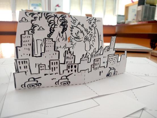 Primer plano de una tarjeta desplegable en B/N con Godzilla arrasando la ciudad.