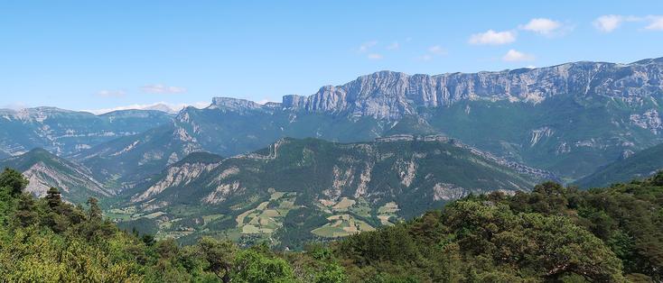 View of two rocky mountain chains behind each other witch trees in the foreground.
