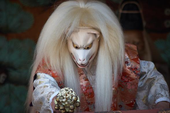 A long-haired Japanese fox spirit looks down during a performance at Asakusa Shrine.