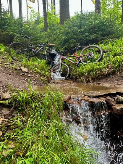 Ein Wasserfall mit Trail von links nach rechts auf dem Wasser steht. Zwei MTBs legen am Hang