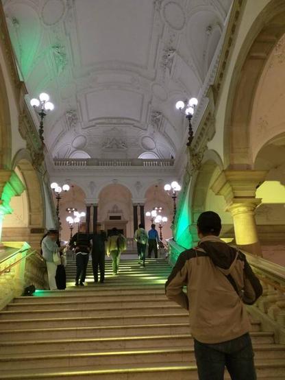 Foto: Menschen im Hauptgebäude der Universität Wien, Stiegenhaus Richtung Großer Festsaal. Für die "Lange Nacht der Forschung" wird die übliche weiße Beleuchtung durch gelbe und grüne Lichtspots ergänzt.