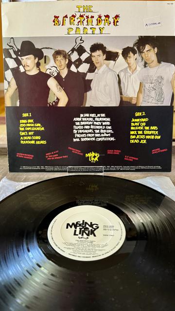 Back album cover. 

Another picture of the band, this time clear and in color. Top third is white with "The Birthday Party" written in yellow block lettering. Lower third below band photo is track listing and credits. White and yellow text on black background

Below is 12" black vinyl disc with white label with large black letters that read "Missing Link"