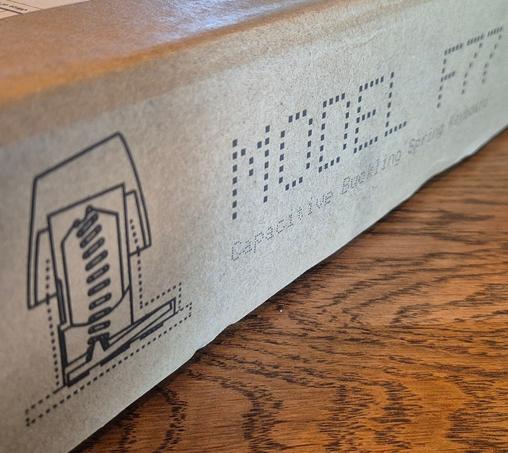 A brown cardboard box on wooden table with a technical drawing of a buckling spring keyboard mechanism on it. The box says Model F77, it's the name of the keyboard inside.