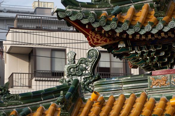 The traditional green and orange roof of the gate gleams in the afternoon light, electric wires and apartments standing just outside.