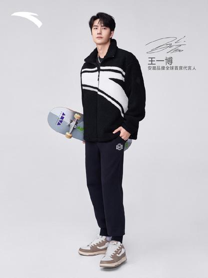 Anta ad image with Wang Yibo wearing a black and white skating outfit, and holding a skateboard under one arm.