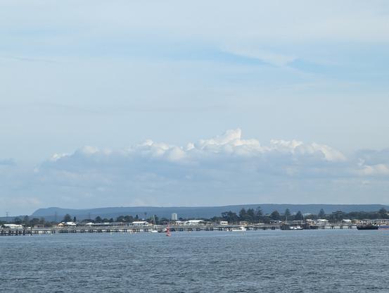 Kurnell's petroleum pier and shoreline with the RNP in the background under a long white cloud