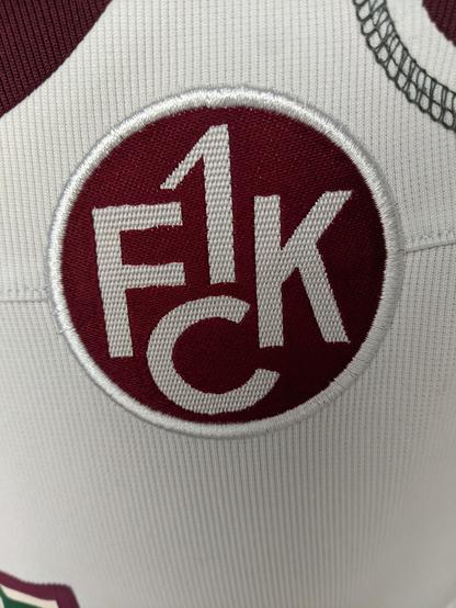 Foto des alten Wappens des 1. FCK Kaiserslautern auf einem Trikot. Ein weißer Schriftzug 1.FCK auf rotem Grund.