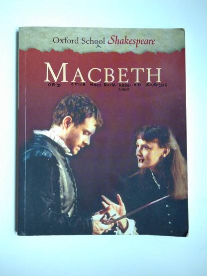 Buchcover. Text oben „Oxford School Shakespeare“, das Doppel-O habe ich zu Augen eines traurigen Smileys gemacht.
Darunter der Titel. Jeden Buchstaben habe ich darunter ergänzt: „Mord. Action. Chaos. Brutal. Erbrechen. Tod. Hirnrissig.“
Darunter links ein Mann in historischer Kleidung. er steht nach rechts, schaut runter auf seine Hände, die einen langen, schmalen metallenen Gegenstand halten. Rechts steht eine Frau, die ihn anschaut. Ihr wurden mit schwarzem Fineliner Vampirzähne gemalt und die Augen rot gefärbt. Er hat im Nacken zwei rote Punkte wie ein Vampirbiss.