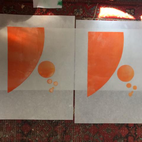 Two prints drying on the floor carpet. Each print is on white kozo paper, 30 cm by 40 cm and is printed in a gradient of orange to paler yellow-orange. The prints show a large section of a circle on the upper left through a smattering of smaller circles of various sizes trending to the lower right.