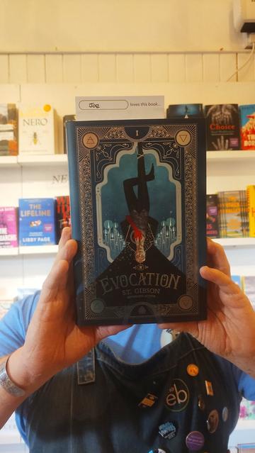 Bookseller Joe holding up Evocation by S.T. Gibson, to recommend it in the Edinburgh Bookshop