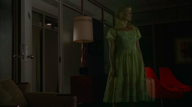A woman stands in an office holding a suitcase. She is semi transparent, like a ghost or a dream