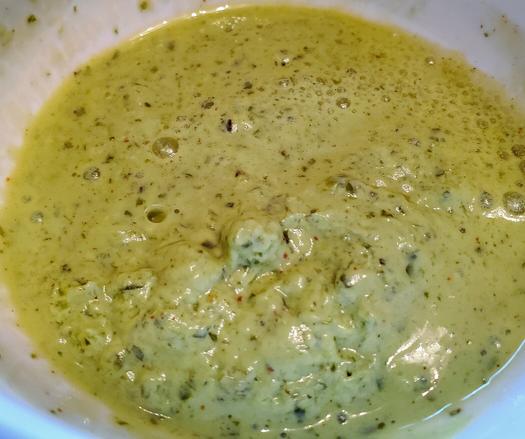 Pudina chutney in a white bowl. Avocado green in colour with specks of assorted spices. It's about as thick as hummus.
