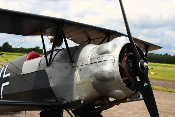 The front of a single-seat open-cockpit "Bücker Jungmeister" vintage biplane with dark grey livery with a typical radial-engine cowling and black propeller