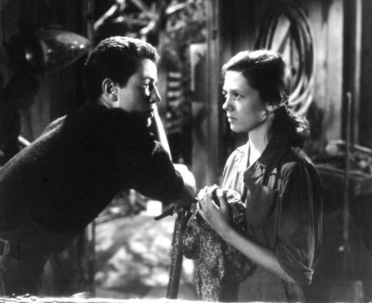The image features two characters from the film "The Farmer's Daughter," portrayed by Cathy O'Donnell and Farley Granger. In this scene, they are in a setting that appears to be a dilapidated barn or a workshop. They are positioned close to each other, with one character leaning in towards the other, as if sharing an intimate moment or a secret. The characters' expressions and body language suggest a sense of tension or a significant exchange between them. Both actors appear to be dressed in period costumes suitable for their roles in the film.